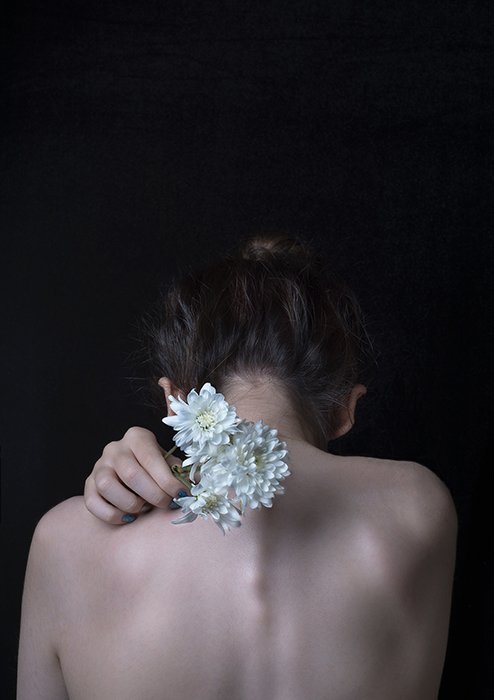 Retrato artístico de la espalda de una modelo femenina sosteniendo flores blancas hacia la cámara