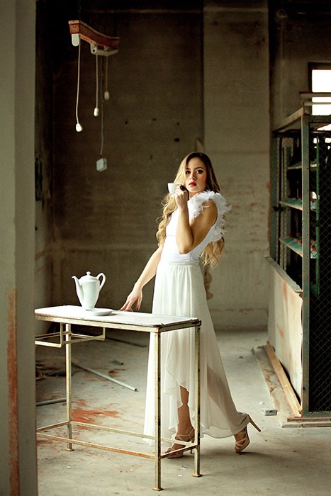 Retrato artístico de una mujer rubia posando en un área de cocina mínima con vestido de noche blanco