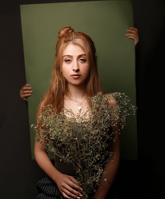 Una chica pelirroja posando con flores sobre un fondo verde: consejos para la fotografía de retratos artísticos