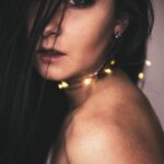 Atmósfera retrato de una mujer de cabello oscuro posando con luces de hadas alrededor de su cuello