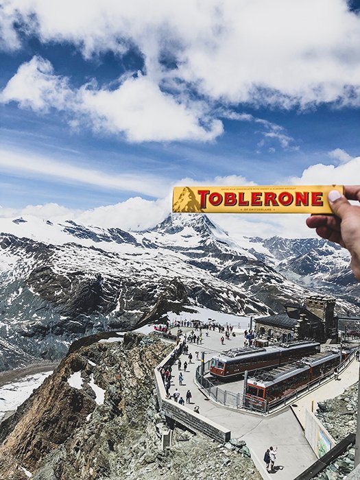 Una persona que sostiene una barra de chocolate toblerone sobre un paisaje montañoso