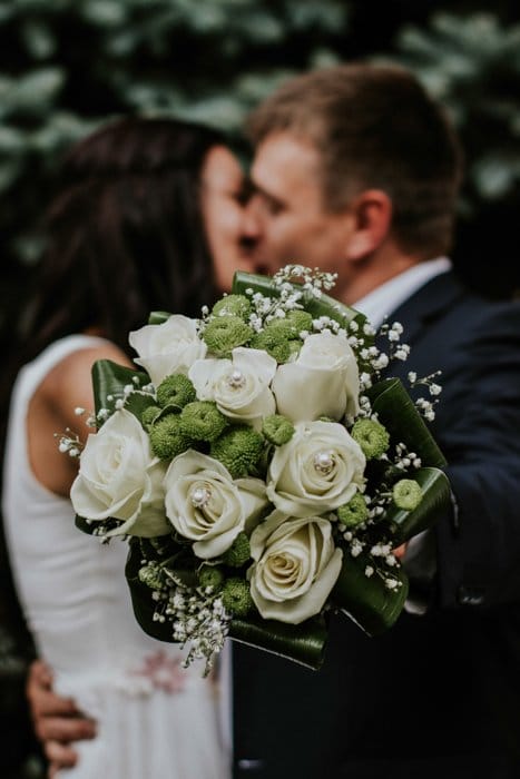 Retrato artístico de una pareja de recién casados ​​sosteniendo un ramo de flores hacia la cámara - fotografía de bodas de bellas artes