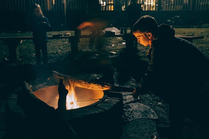 Un retrato con poca luz de un niño colocando palos en un fuego al aire libre