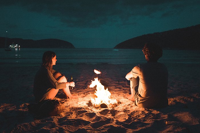 Una pareja sentada junto a una hoguera en la playa por la noche - fotos de hogueras