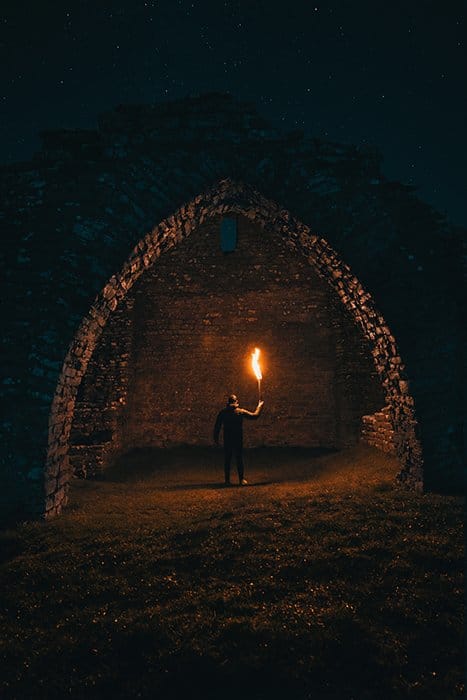 Un retrato dramático y misterioso de un hombre que sostiene una llama debajo de un arco por la noche: consejos para la fotografía de incendios
