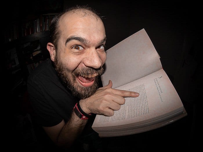 Retrato humorístico de un hombre apuntando a un libro filmado con una lente ojo de pez