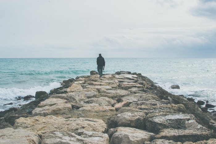 foto luminosa y aireada de un hombre caminando hacia el mar en un muelle rocoso - fotografía de punto focal