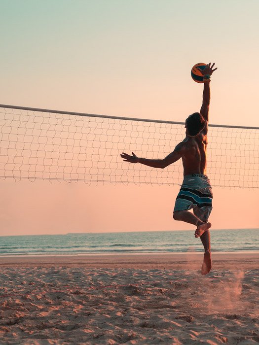 Un retrato de una persona jugando voleibol en la playa al atardecer.
