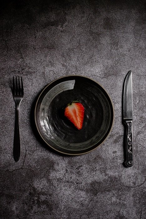 Una fresa en rodajas en un plato negro y con un tenedor y un cuchillo utilizados como accesorios de fotografía de alimentos