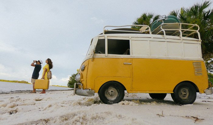 Una pareja en una playa con una camioneta amarilla detrás de ellos