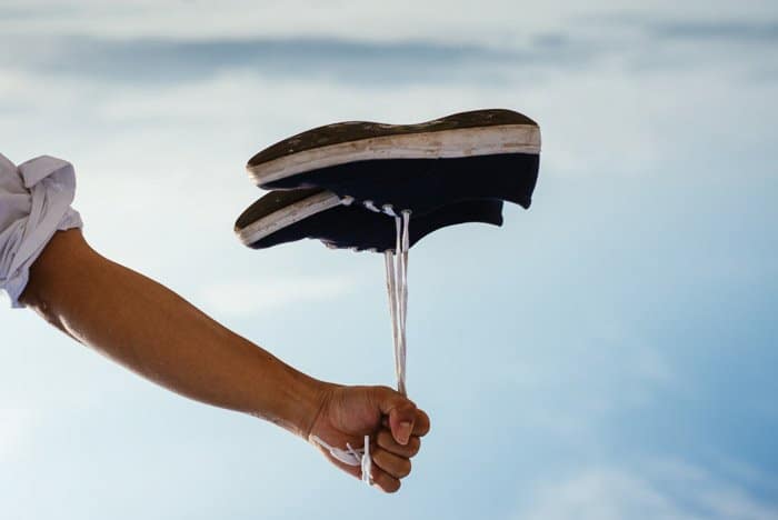 Una persona sosteniendo un par de zapatos por los cordones que parecen flotar como un globo