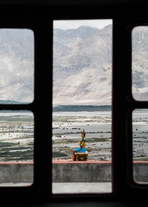 Foto de una estatua budista tomada desde una ventana con montañas al fondo