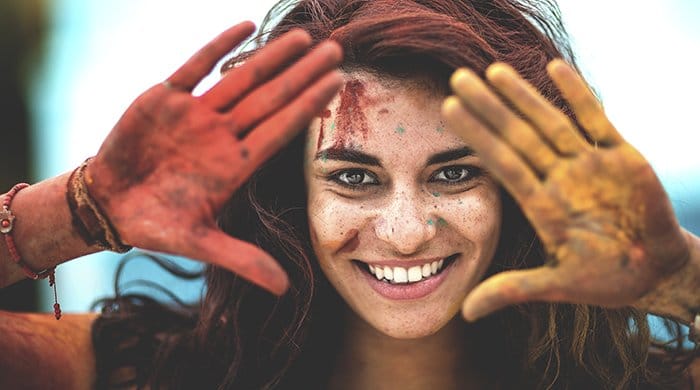 Mujer joven sosteniendo las manos cubiertas de pintura para enmarcar su rostro.