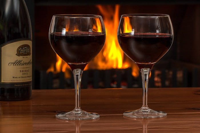 Una foto de una botella de vino y dos copas con un fuego de fondo