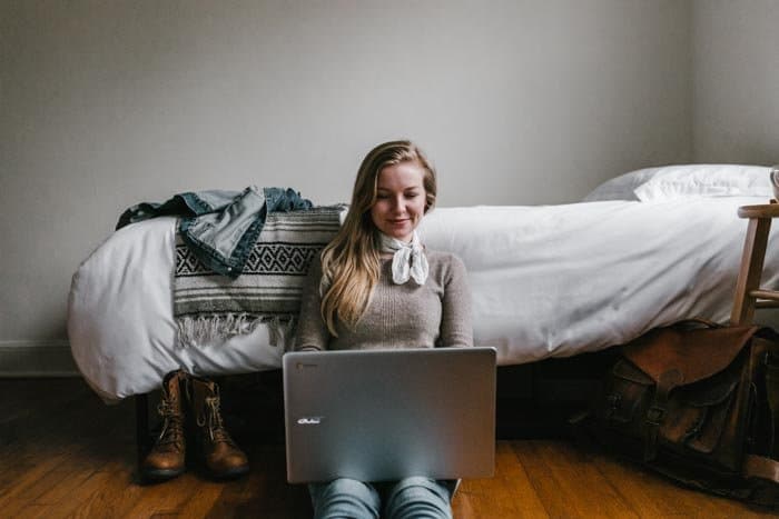 Una niña sentada en el piso de un dormitorio editando fotos en una computadora portátil