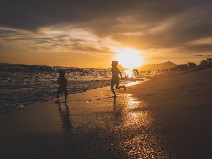 Dos niños pequeños corriendo en una playa con poca luz