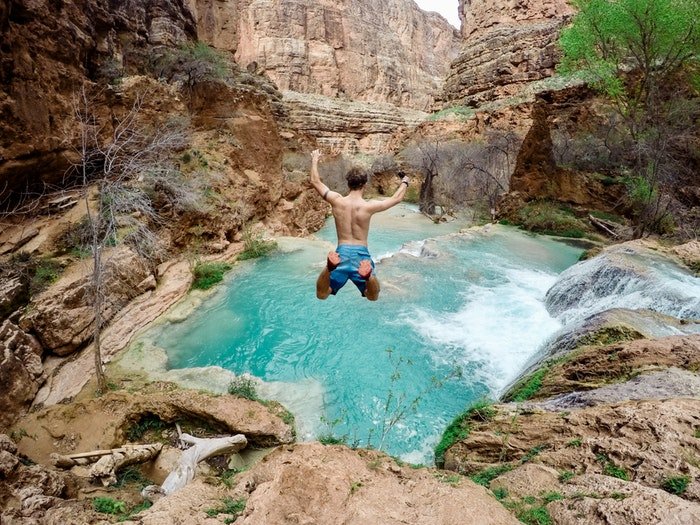 Hombre saltando a un charco de agua rodeado de montañas rocosas