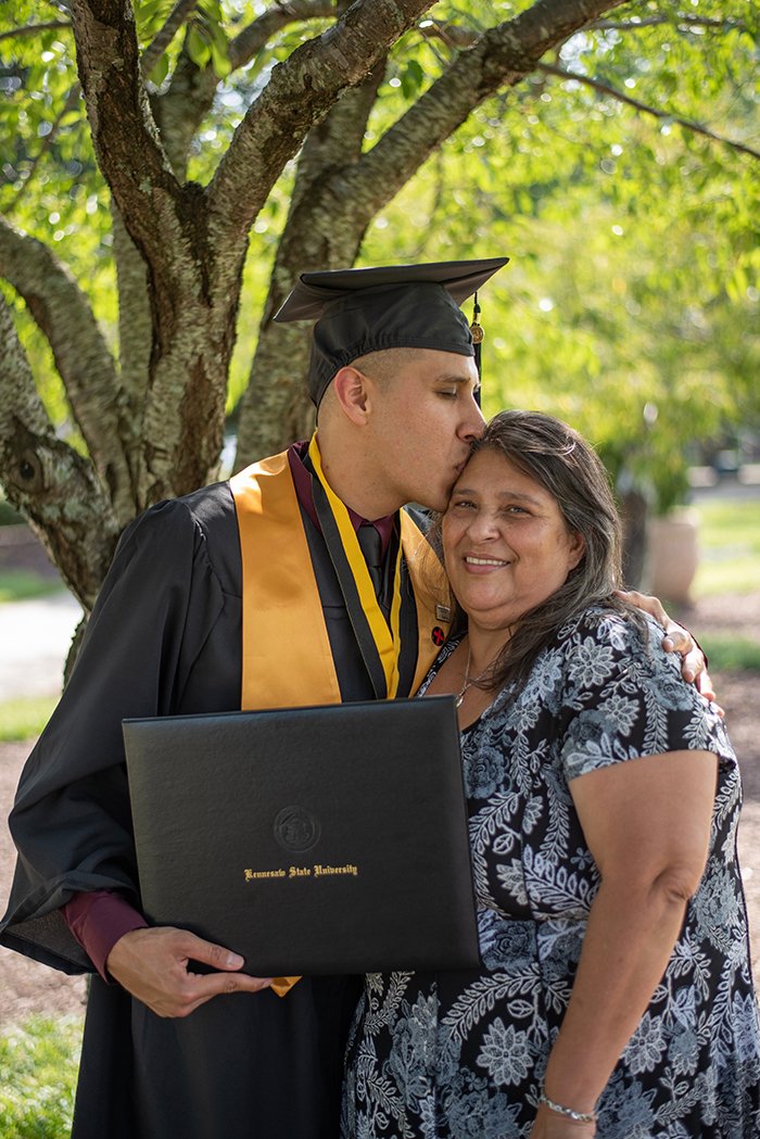 Hermoso retrato de graduación de un estudiante varón abrazando a su madre al aire libre