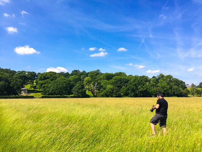 hombre con una cámara caminando por un campo de hierba verde brillante bajo un cielo azul profundo