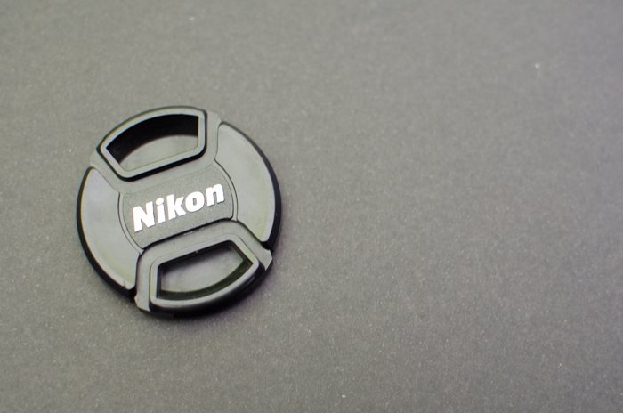 Una tapa de lente Nikon sobre fondo gris - fotografía de tarjeta gris