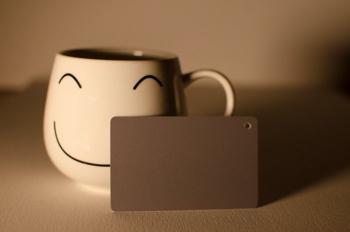 Una taza de cara sonriente sobre un fondo neutro junto a una tarjeta gris de fotografía para equilibrar el color