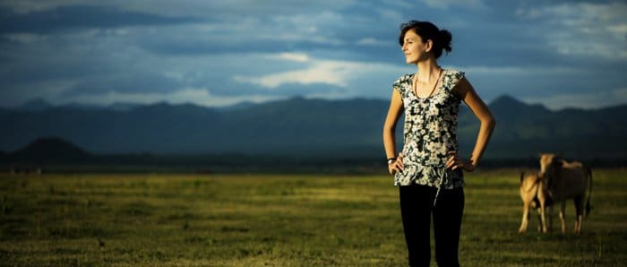 Foto de una mujer al aire libre con vacas y montañas al fondo.