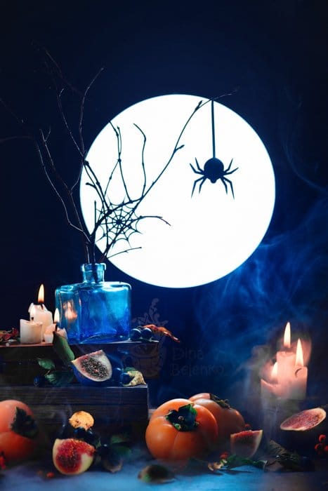 Un bodegón aterrador con la silueta de una araña, una luna llena, velas y otros accesorios espeluznantes.