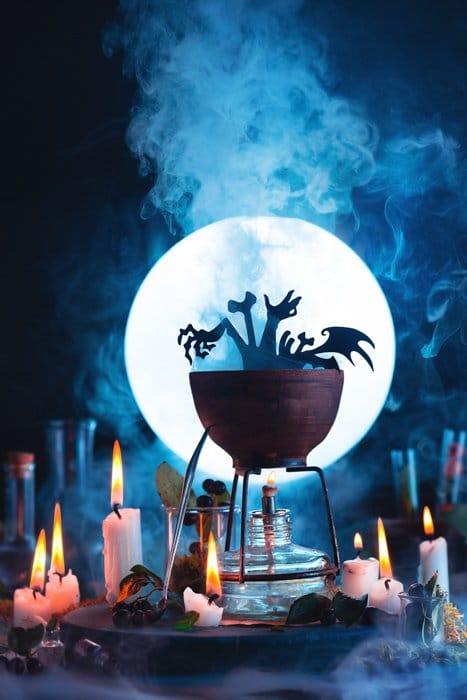 Bodegón atmosférico de Halloween con un caldero, una luna llena, velas y otros accesorios espeluznantes