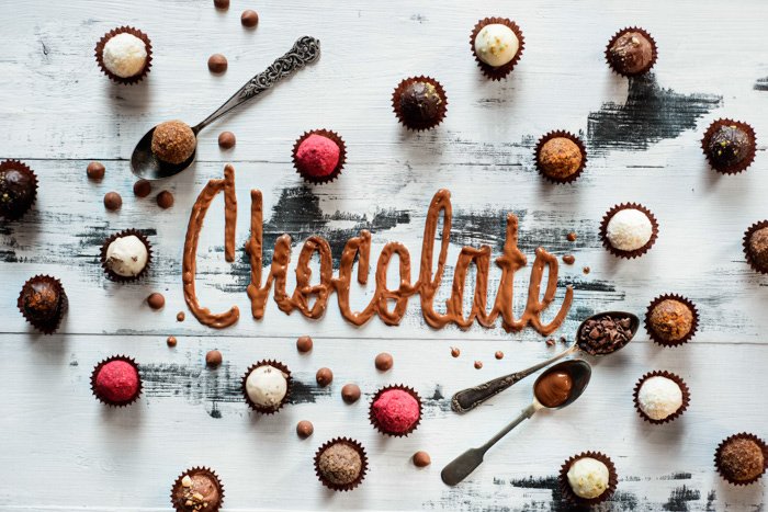 Un plano creativo de chocolates y la palabra 'chocolate' escrito con tipografía de alimentos fondo pintado a mano
