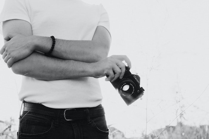 Torso de un fotógrafo con una camiseta blanca y sosteniendo una cámara