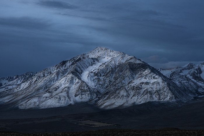 Un pico de montaña nevado con un cielo oscuro.