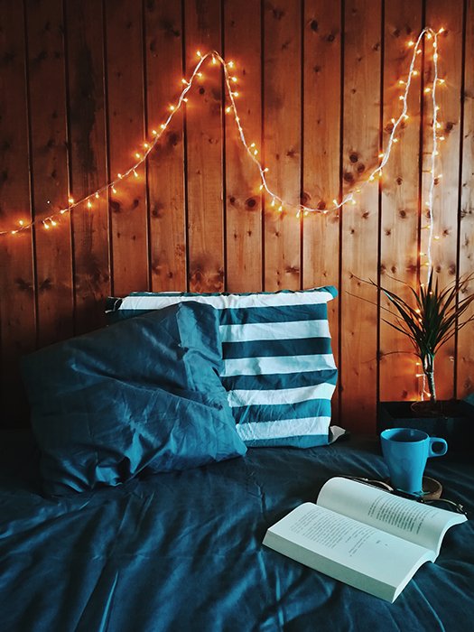 Una foto de naturaleza muerta de un libro y una taza en una cama con luces de hadas en la pared - fotografía de luces de hadas