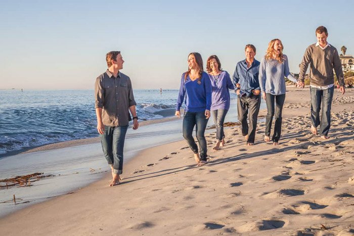 Una linda sesión de fotos familiares en la playa con la familia caminando cerca de la orilla con atuendos coordinados