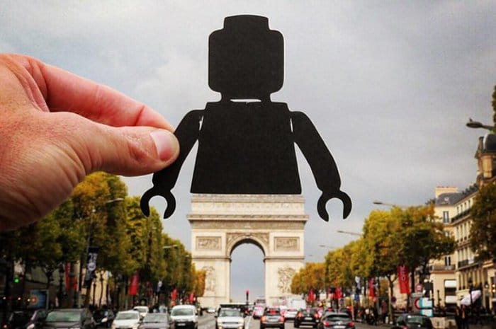 una genial foto en perspectiva forzada de una persona sosteniendo la silueta de una figura de Lego sobre el Arco del Triunfo en París