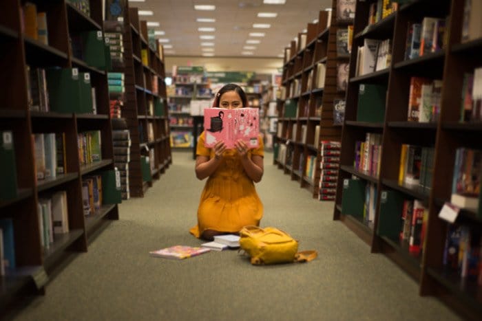Retrato conceptual de una niña leyendo en el piso de una biblioteca tomada con fotografía de lente libre