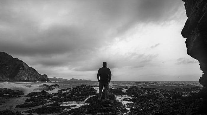 Una bella fotografía en blanco y negro de un hombre en una playa mirando hacia el océano