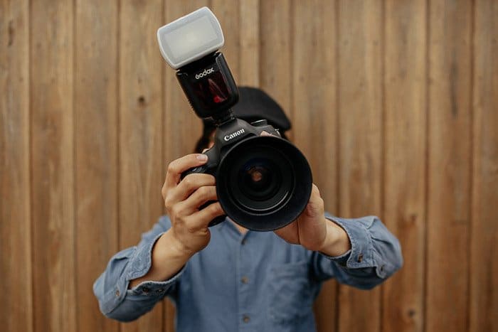Un fotógrafo sosteniendo una cámara réflex digital con un difusor de flash adjunto