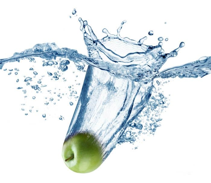 La manzana verde cae profundamente bajo el agua con un gran chapoteo.