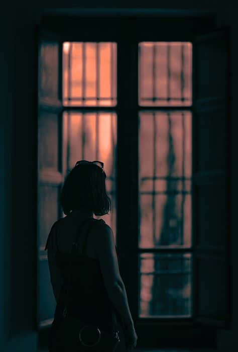 Moody escena de una chica mirando por la ventana en una habitación oscura