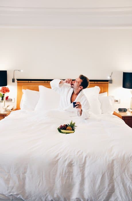 Un hombre en la cama de un hotel comiendo de un plato de frutas frescas