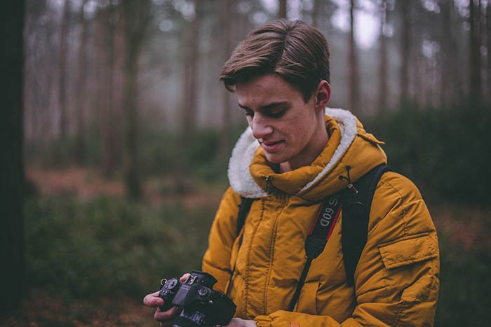 fotógrafo masculino con una chaqueta de invierno amarilla y configurando su cámara