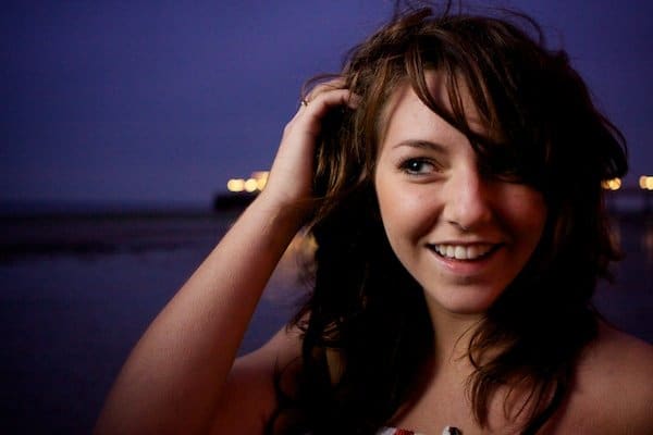 Cierra la fotografía de retrato de una chica con las manos en el pelo en una playa.  Fotografía crepuscular.