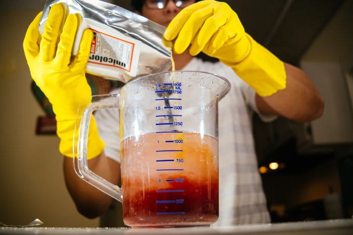 una imagen de un hombre con guantes amarillos mezclando productos químicos de revelado de película en una taza medidora de vidrio