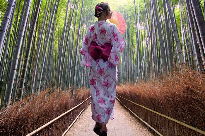Una chica con traje tradicional japonés caminando por un bosque de bambú