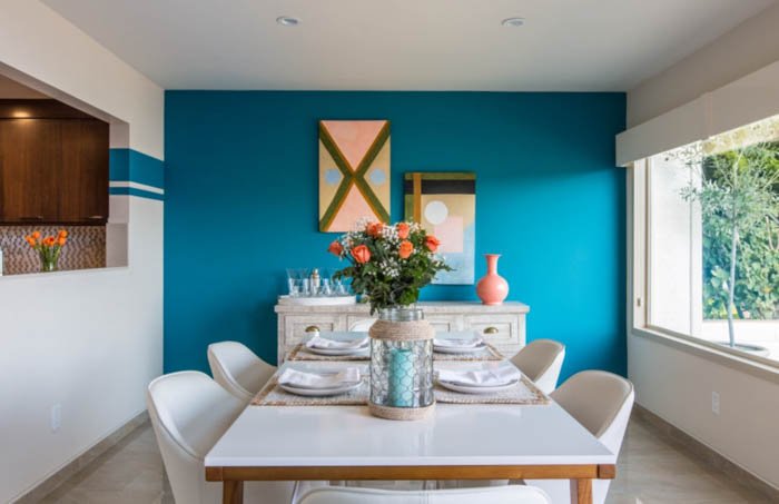comedor soleado con muebles blancos y una pared azul al fondo