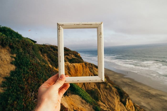 Una persona que sostiene un marco de imagen frente a un paisaje.
