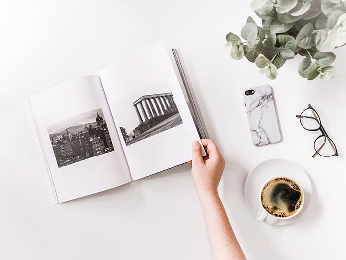 Un plano artístico de un fotolibro genial, una taza de café, vasos y un teléfono inteligente en una mesa blanca: cómo hacer su propio fotolibro para hacer su propio fotolibro