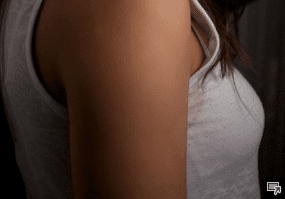 El hombro de una mujer con una camiseta sin mangas blanca.