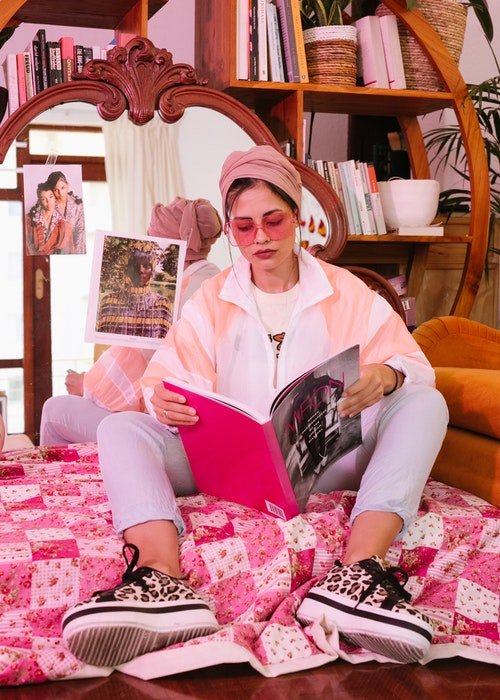 una imagen de una mujer sentada en el suelo leyendo una revista con gafas de sol oink en