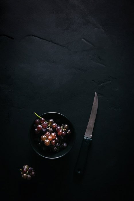 Fotografía cenital de uvas en un recipiente junto a un cuchillo